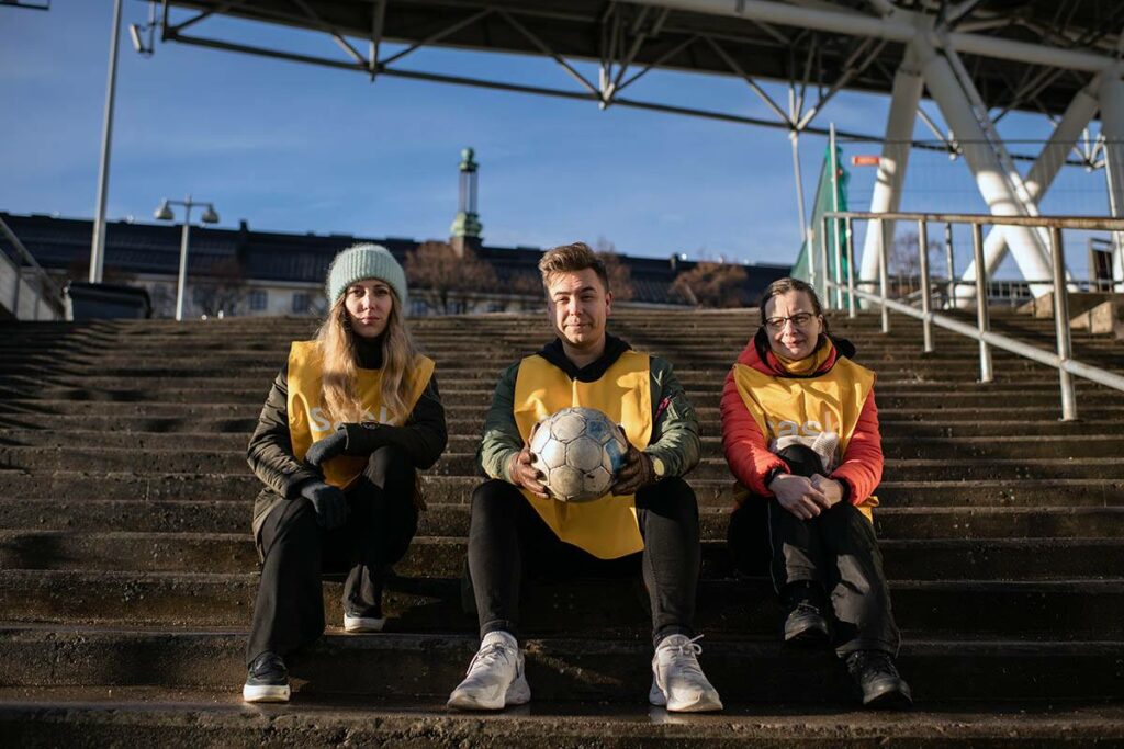 SASK-lähettiläät Vanessa Westerlund, Uula Neitola ja Katri Korhonen istuvat portailla.